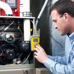 Technician working on HVAC equipment, measuring system components for maintenance at Great Day Plumbing & Air.