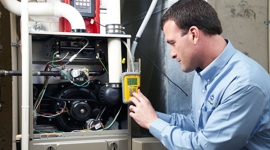 HVAC technician inspecting a furnace with a multimeter during maintenance at Great Day Plumbing & Air.