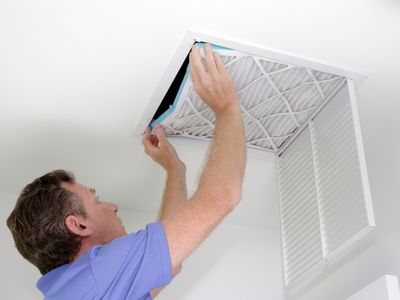 Man replacing air filter in HVAC system, emphasizing routine maintenance for improved efficiency and longevity.