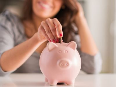 Woman depositing a coin into a pink piggy bank, symbolizing savings and financial planning.