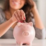 Woman depositing coins into a pink piggy bank, symbolizing savings for home maintenance by Great Day Plumbing & Air.