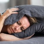 Woman holding a grey pillow in a bedroom, reflecting distress, related to plumbing and HVAC service challenges.