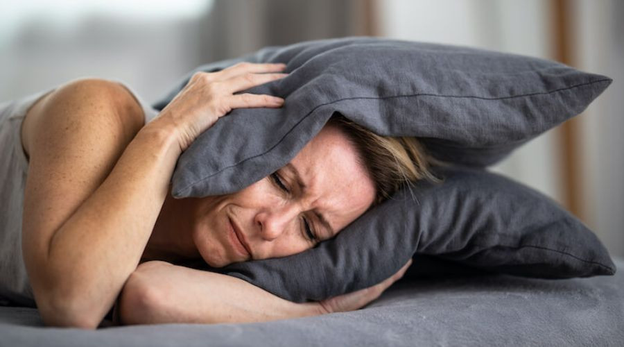 Distressed woman shielding her face with pillows in a muted indoor setting, conveying emotional pain.