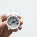 A white alarm clock held in a hand, indicating 12:00, symbolizing timeliness for Great Day Plumbing & Air services.
