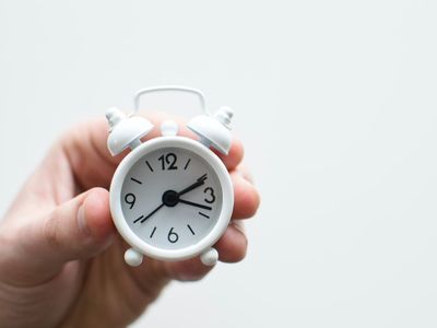 Hand holding a white alarm clock symbolizing time-saving benefits of hiring professional HVAC services over DIY repairs.