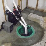 Green sump pit with pumps and white PVC pipes for water management in a basement by Great Day Plumbing & Air.