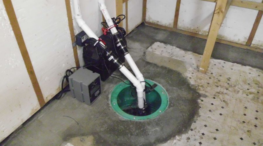 Green sump pump system in a basement, featuring white PVC pipes and plumbing components by Great Day Plumbing & Air.