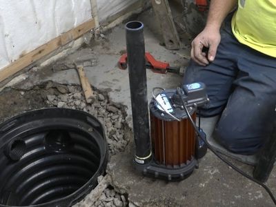 Sump pump installation in a basement, showcasing the pump unit beside a sump pit, emphasizing plumbing solutions for flood prevention.