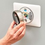 Hand adjusting a round thermostat with visible wires, part of HVAC systems by Great Day Plumbing & Air, Wilmington, NC.