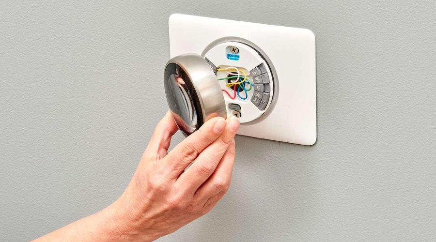 Hand adjusting a circular thermostat unit with visible wires for energy management by Great Day Plumbing & Air.