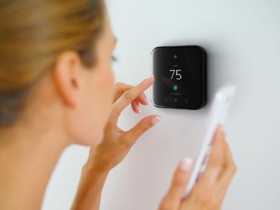 Woman adjusting a smart thermostat reading 75 degrees, highlighting potential issues with temperature accuracy in HVAC systems.