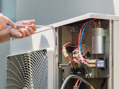 HVAC technician repairing air conditioning unit, showcasing electrical components and tools, emphasizing maintenance and efficiency for summer cooling.