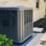 Air conditioning unit on a flat surface with landscaping and a building wall, representing Great Day plumbing services.