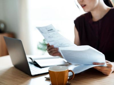 Woman reviewing utility bills at a desk with a laptop and coffee cup, reflecting on financial decisions related to heater efficiency and costs.