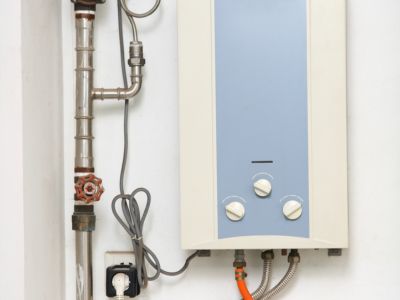 Tankless electric water heater mounted on a wall, featuring control knobs and connected pipes, illustrating efficient water heating solutions discussed in plumbing services.